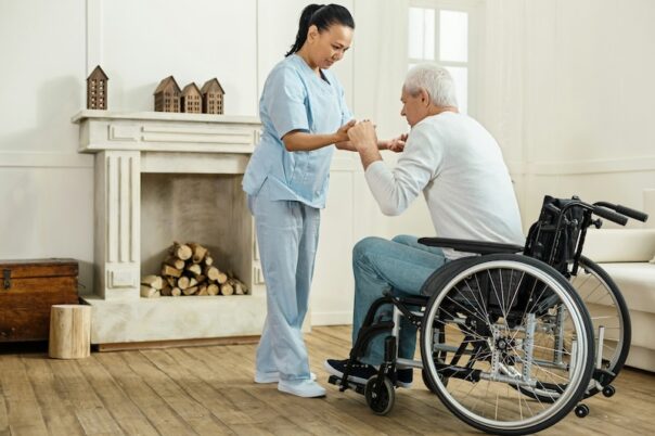 elderly man at home in being helped out of his wheelchair by his nurse